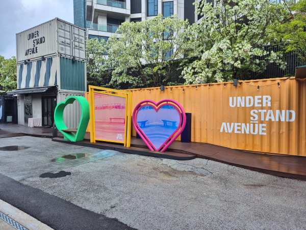 언더스탠드에비뉴의 다채로운 색상의 하트 모양 포토존과 주변의 푸른 나무들
