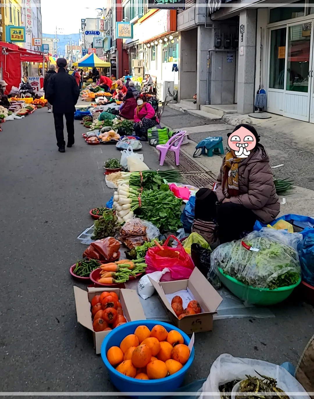 시장할머니 6명이 바닥에 앉아있고 그앞에는 무, 시금치, 뻥튀기, 단감, 곶감, 파가 놓여 있음