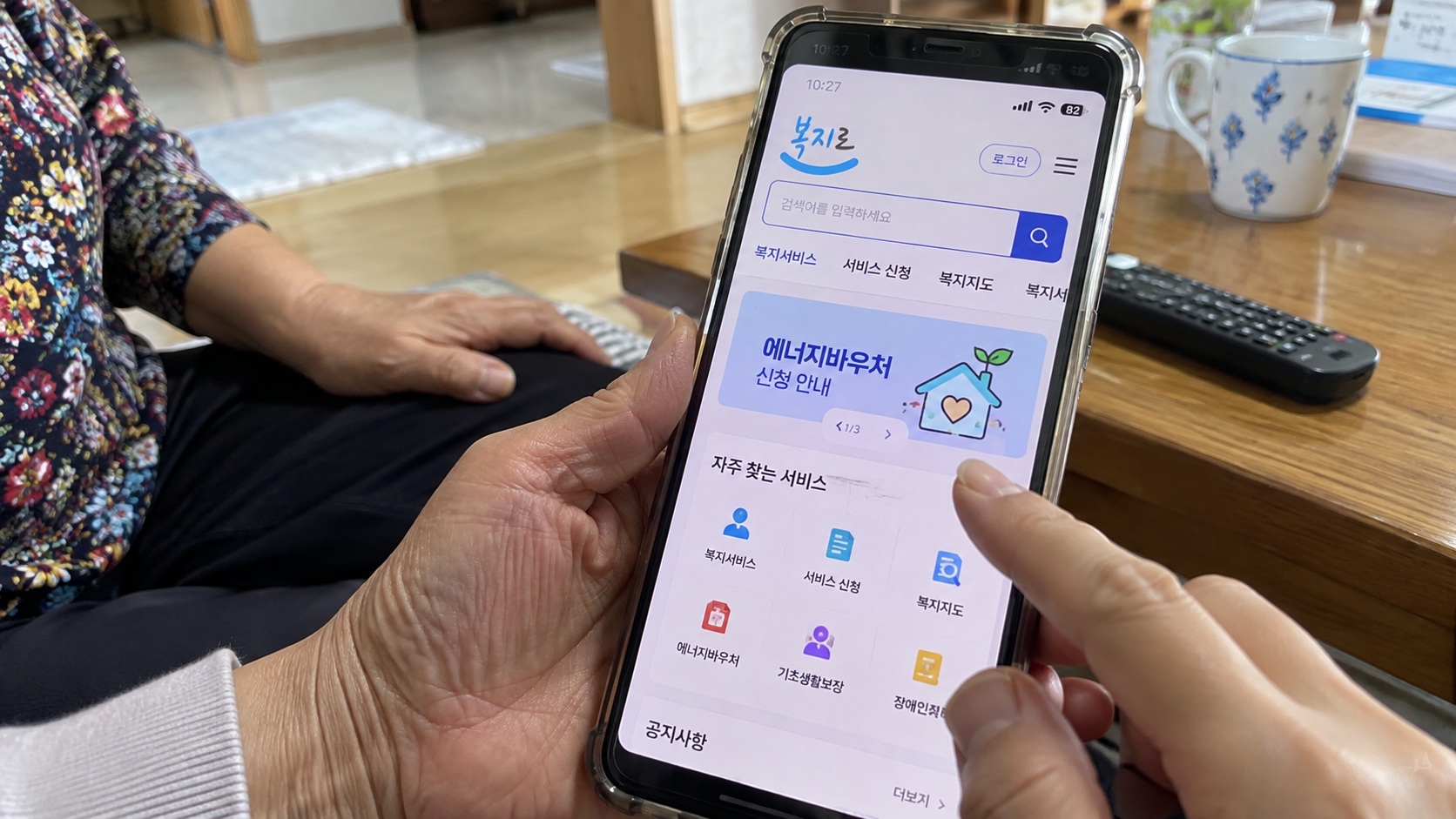 부모님과 함께 스마트폰 복지로 화면에서 에너지바우처 신청 안내와 복지서비스를 확인하는 모습