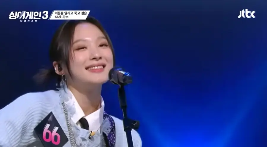 싱어게인3- 하늘색 자켓을 입고 기타를 치며 스탠딩마이크 앞에서 미소짓는 66호