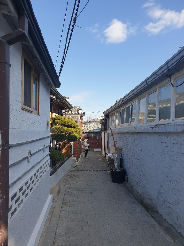파란 하늘 한옥이 들어선 거리. 끝에 누구를 기다리는 행인까지 평화롭다.
