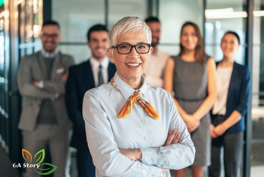 자신감 넘치는 시니어 여성 리더가 젊은 직장 동료들과 함께 서 있는 모습, 나이에 상관없이 도전하는 사람들의 특별한 비밀을 보여주는 이미지 via canva