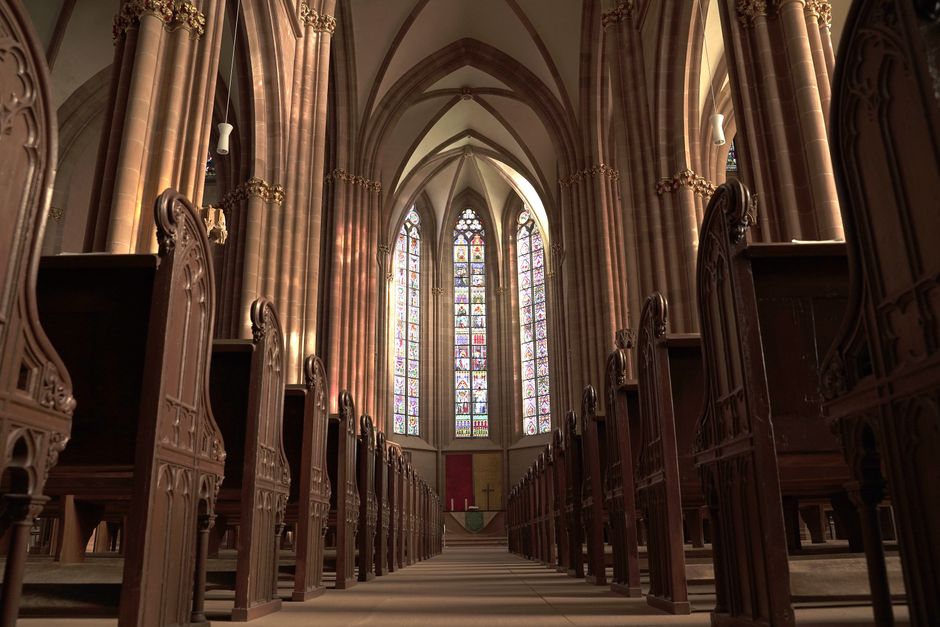 Interior view of a gothic church in Oppenheim, showcasing arches, pews, and stained glass windows.