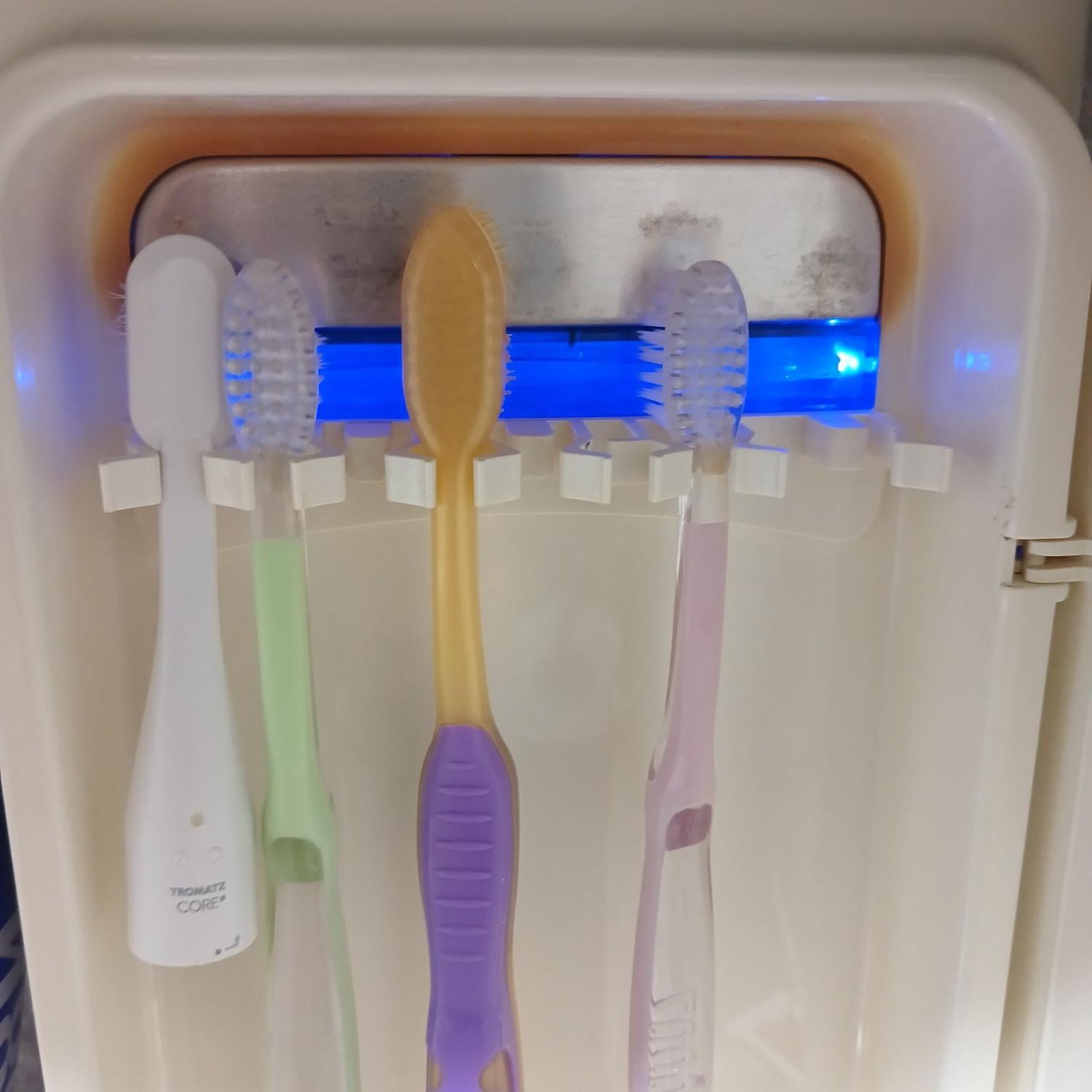 가정용 칫솔 살균기 내부에 칫솔 4개가 거치되어 있으며, UV LED 램프 일부가 고장 나 중앙 부분이 어두운 모습