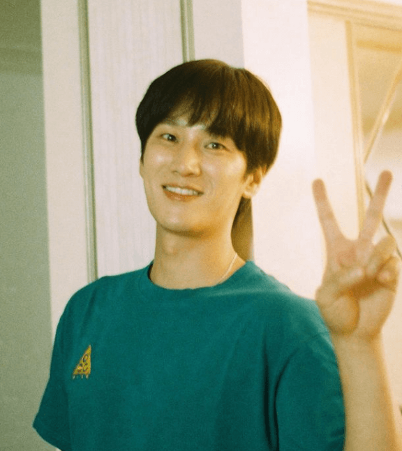 초록색 티셔츠를 입고 손가락으로 브이를 만들고 사진을 찍는 장면