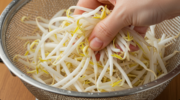 데친 콩나물을 찬물에 재빨리 헹궈 체에 밭쳐 물기를 꾹 짜고 있는 모습