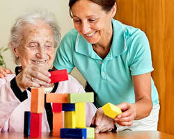 요양보호사가 치매 노인과 함께 블록 쌓기 놀이를 하며 웃고 있는 장면