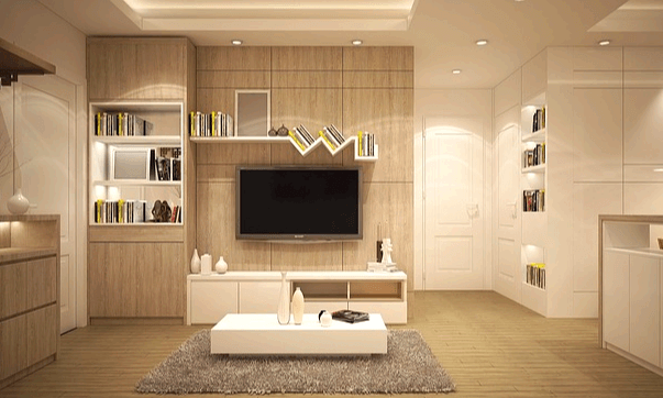 베이지색 가구들이 가득한 거실 풍경이다. 벽걸이형 TV가 있고 책장엔 책들이 많다.