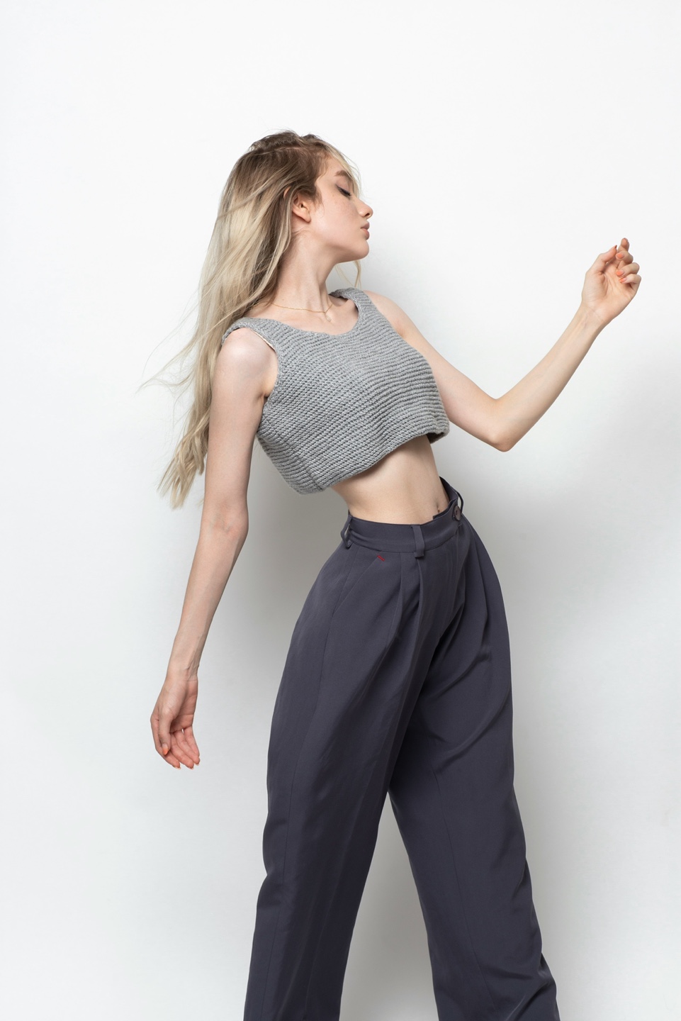 금발 긴머리에 다크그레이의 와일드 바지 크롭 민소매 스웨터를입은 모델 사진