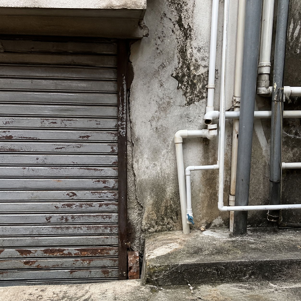 Weathered metal shutters and tangled pipes along an alley wall