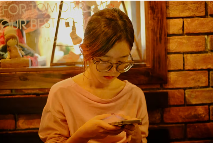 카페에서 스마트폰 화면을 집중해서 바라보는 안경 낀 여성. 요금제 확인이나 알뜰폰 비교를 연상시키는 장면.