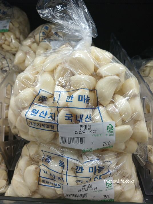 국산 깐마늘이 투명 비닐 포장에 담겨 마트 진열대에 쌓인 모습으로, 가정에서 바로 조리할 수 있는 신선한 생마늘 제품 사진