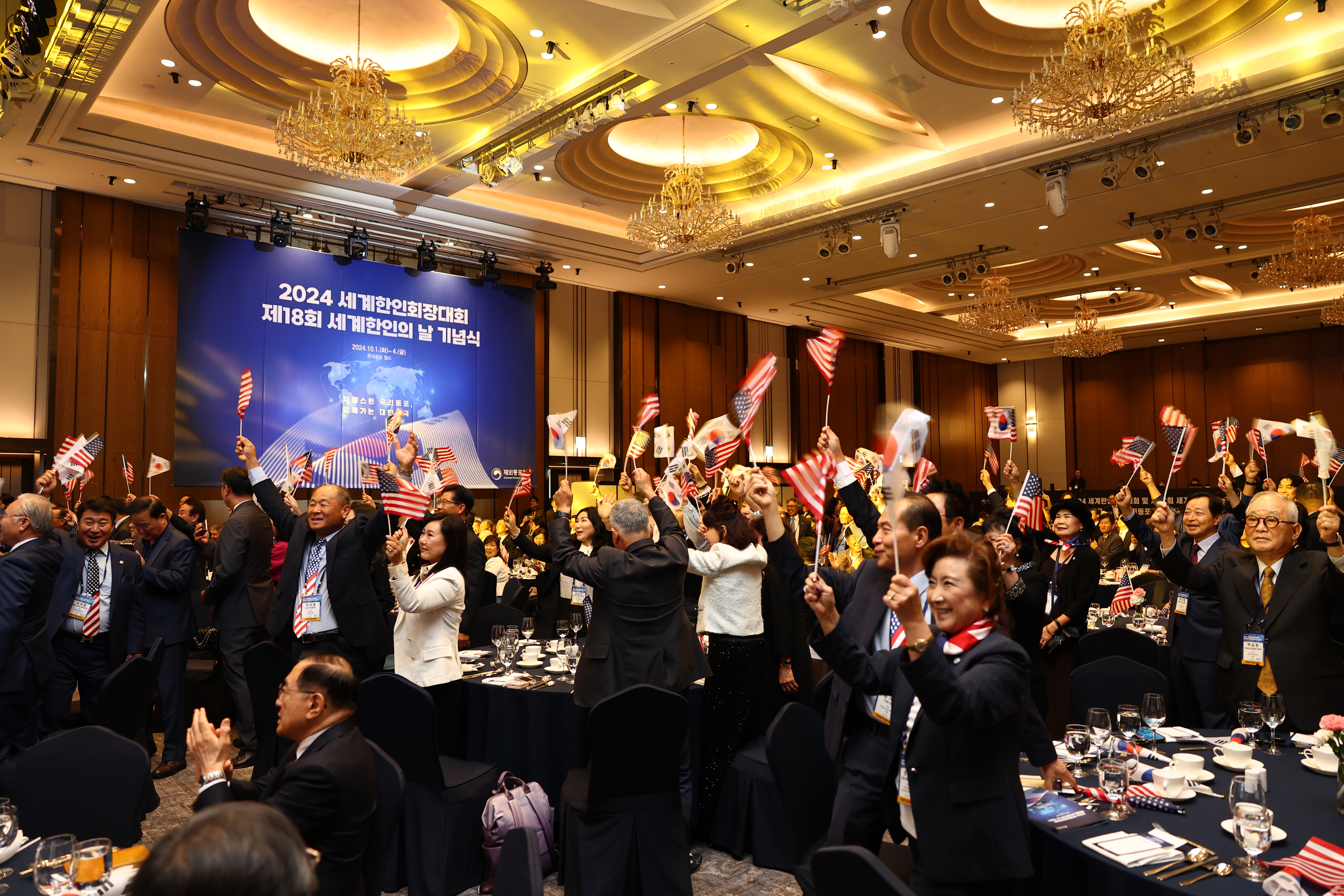2024년 10월 1일 서울 송파구에 있는 롯데호텔 월드에서 열린 2024년 세계한인회장대회 개회식 장면 2, 참석자들이 자리에서 일어나 두 손을 높이 들고 환호하고 있다.