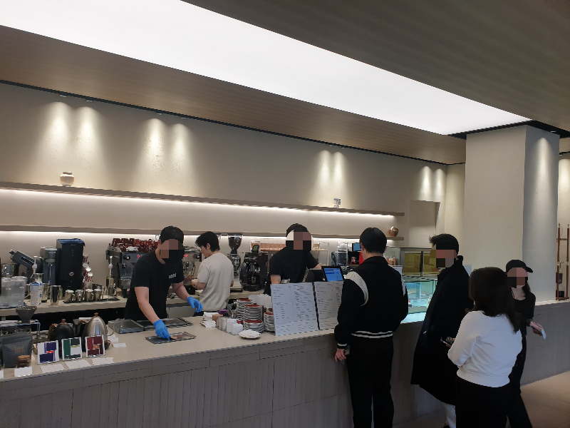 고객들이 줄을 서서 주문 차례를 기다리고 있다. 뒤에는 일하고 있는 직원들이 보인다.