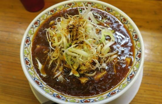 알록달록한 동그란 접시에 진한 갈색의 국물과 잘게 썬 대파가 올라가 있다.