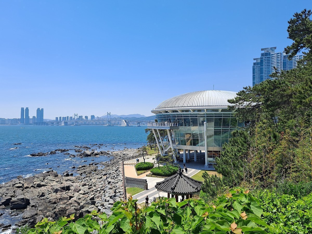 Rocky shore of Dongbaekseom Island with the Nurimaru building and Gwangan Bridge in the distance, Busan