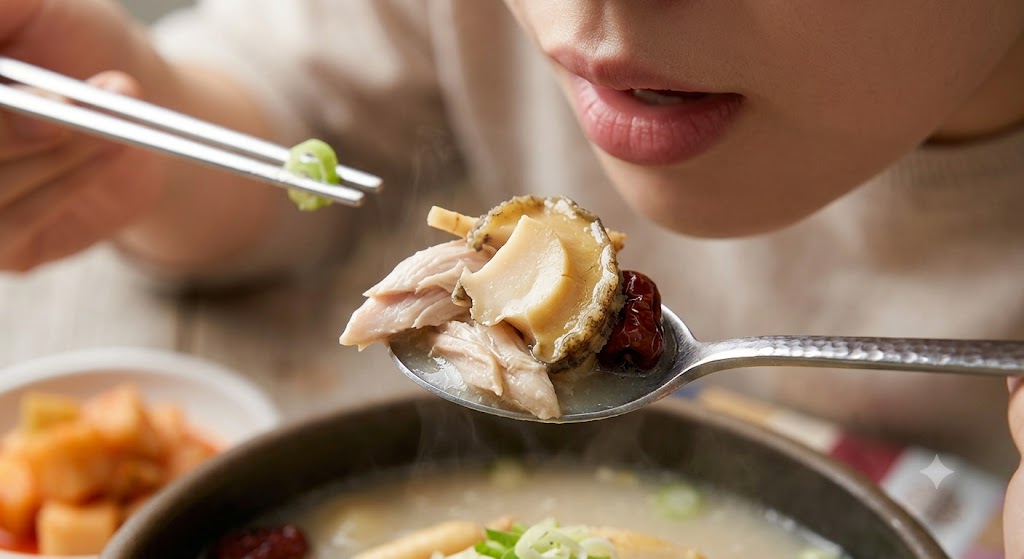 숟가락으로 닭고기와 전복을 가득 떠서 맛있게 먹으려는 모습의 초복 보양식 클로즈업