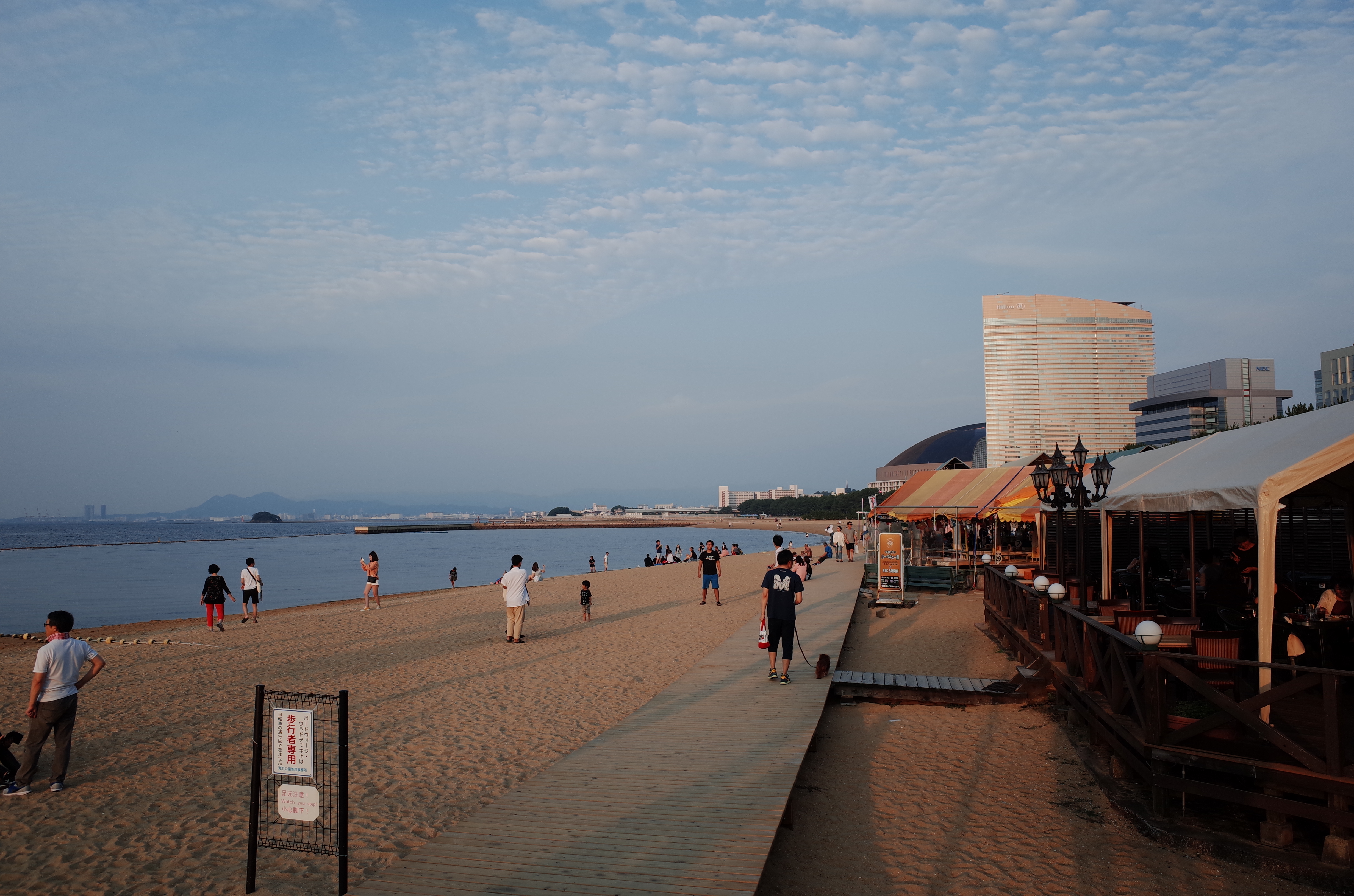 해 질 녘 후쿠오카 모모치 해변의 넓은 모래사장과 나무 데크 산책로, 멀리 보이는 힐튼 호텔과 후쿠오카 야후오쿠 돔 전경.