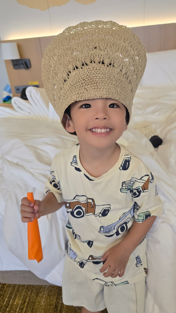 침대에서 아이가 엄마 모자를 거꾸로 쓰고 있는 사진