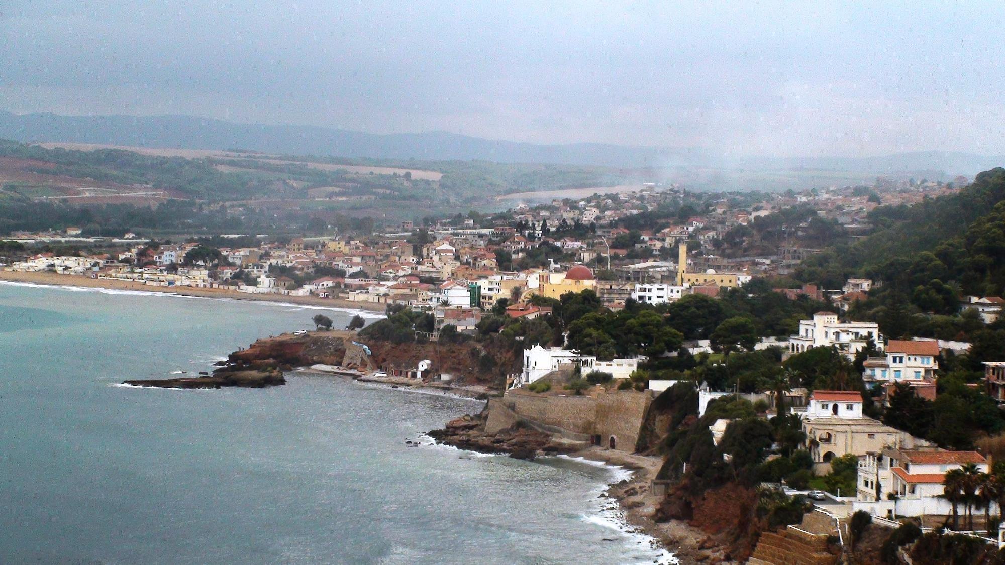 알제리 북부 지중해 연안의 도시 티파사(Tipaza)를 내려다본 전경. 해안선을 따라 주택과 건물이 빼곡히 들어서 있고, 언덕 위까지 도시가 확장되어 있다. 바다와 절벽, 고전적인 건축 양식이 어우러져 고요하면서도 역사적인 분위기를 자아낸다.