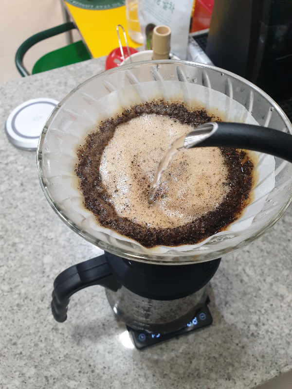 하리오 스위치에 검은색 드립포트로 푸어 중. 원두에 옅은 갈색 거품이 일어나고 있다.