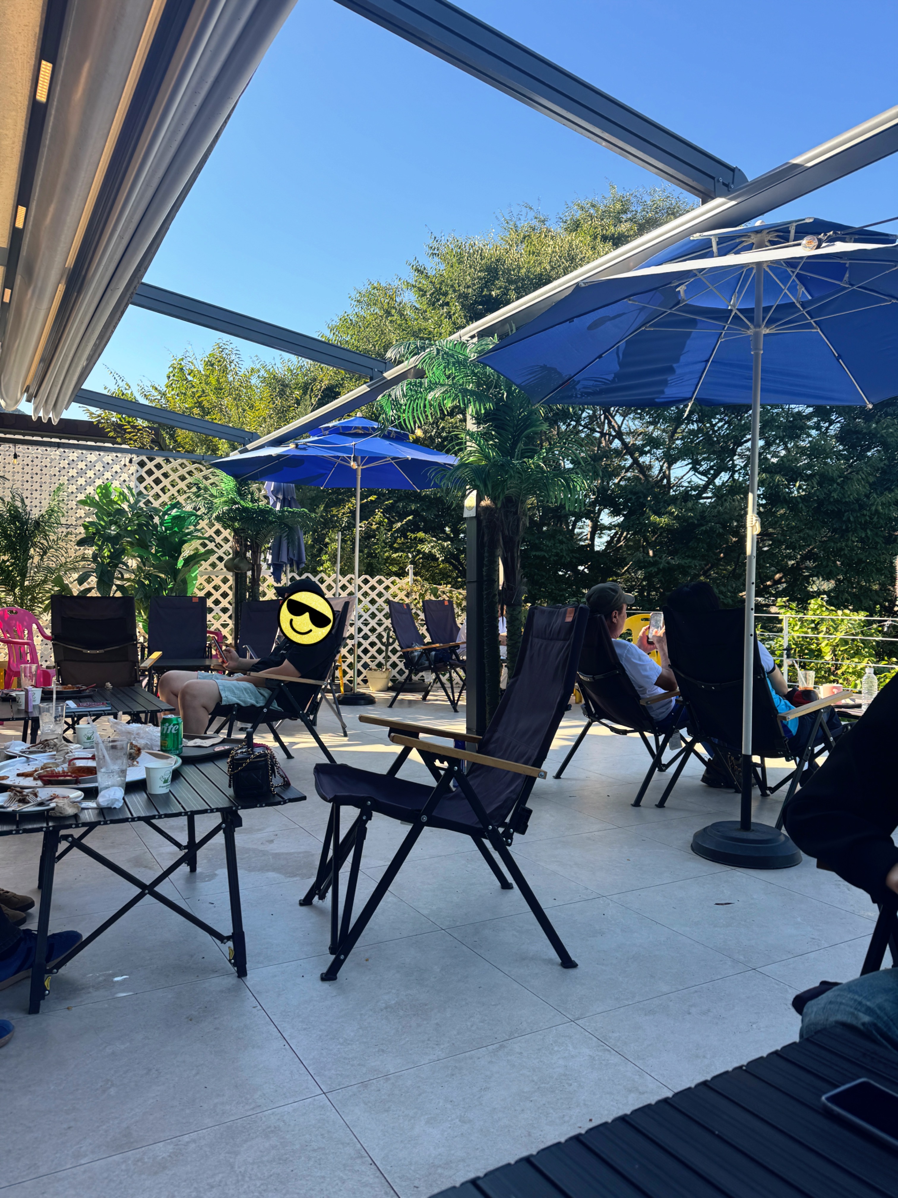 피맥플레이스 팔당점 테라스 전경. 파란 파라솔과 캠핑 체어가 놓인 넓은 야외 공간에서 손님들이 강뷰를 즐기고 있다.