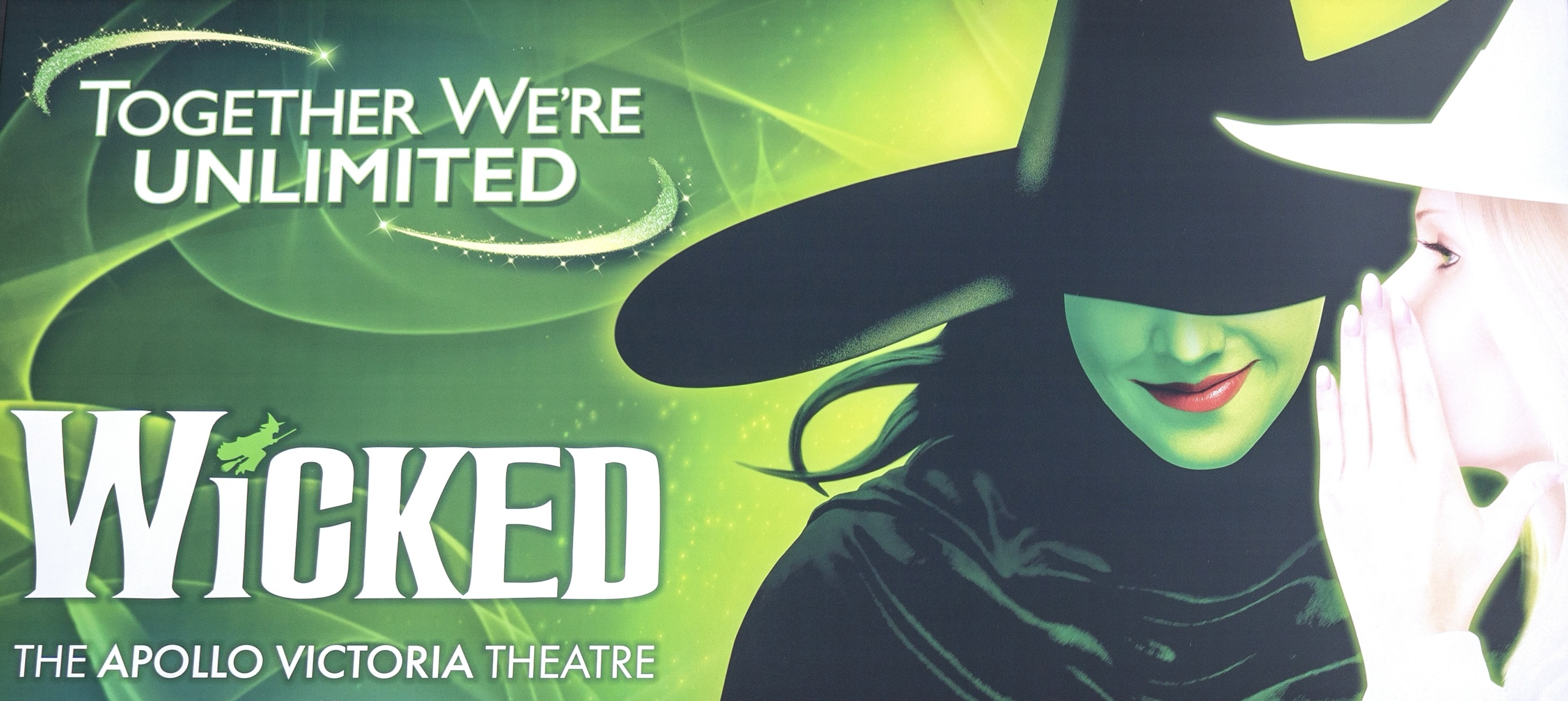 뮤지컬 Wicked의 포스터. 초록색 피부의 마녀와 백색 모자를 쓴 여성이 속삭이는 장면이 그려져 있으며, “Together We’re Unlimited”라는 문구와 함께 아폴로 빅토리아 극장에서 공연 중이라는 정보가 포함되어 있다. 런던 키즈 위크 참가 공연 중 하나이다.