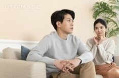 부인이-소파에-앉아-미안해하고-남편은-TV를-보며-냉랭한-모습