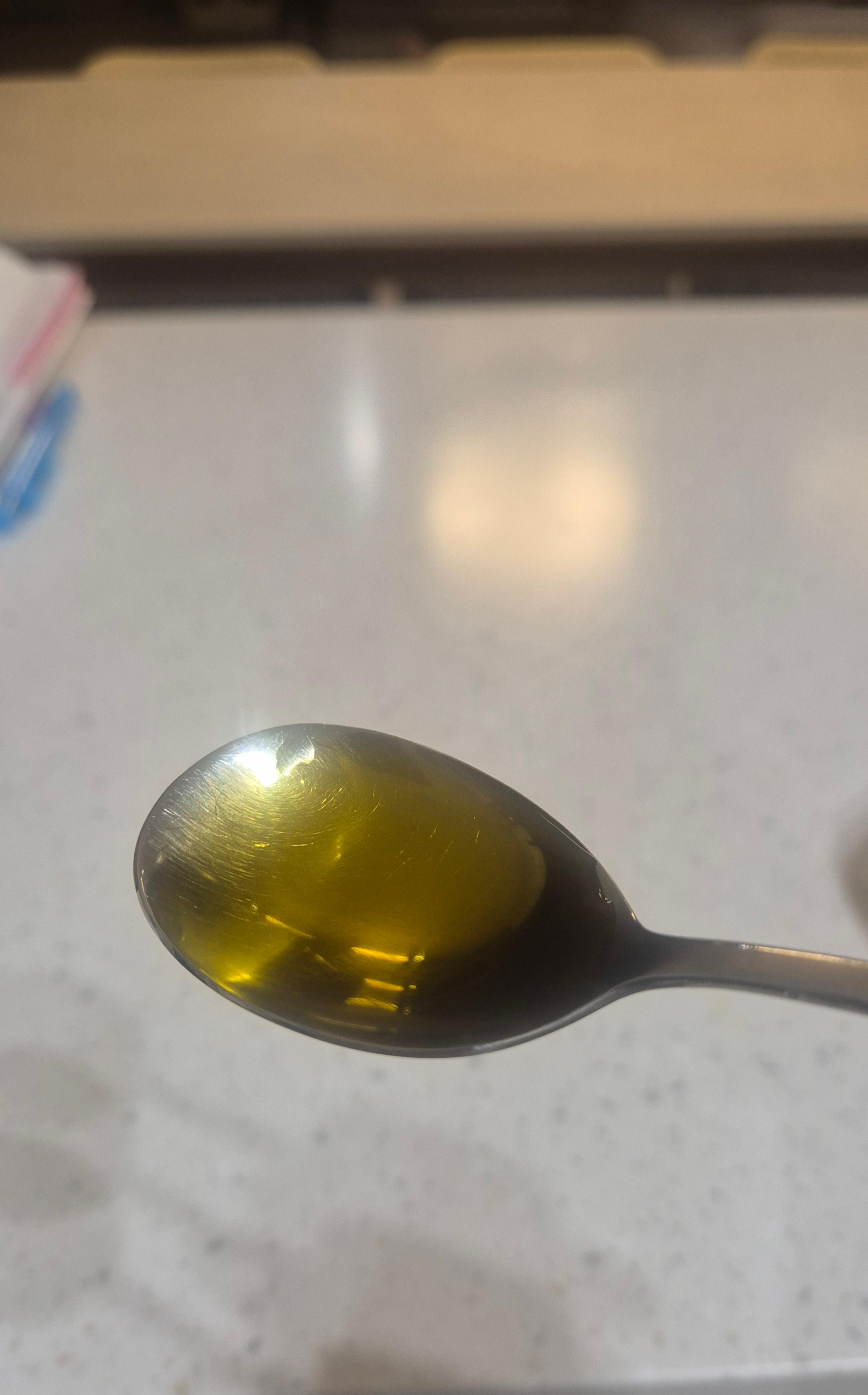 금속 숟가락 위에 가득 담긴 맑고 황금빛을 띠는 엑스트라 버진 올리브오일. 아침 공복 섭취를 위한 한 스푼의 건강 루틴.