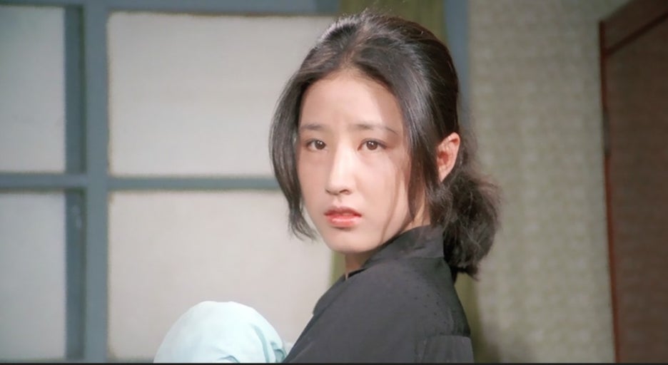 미옥이 무언가를 껴안은 채 뒤돌아보는 장면, 슬픔과 두려움이 뒤섞인 눈빛 속에 감정의 균열이 비치는 순간