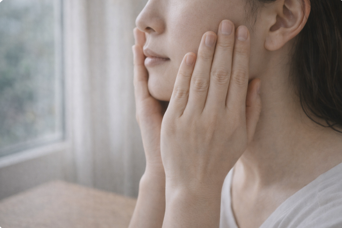 창가에서 양손으로 얼굴을 감싸며 피부 속당김을 느끼는 모습