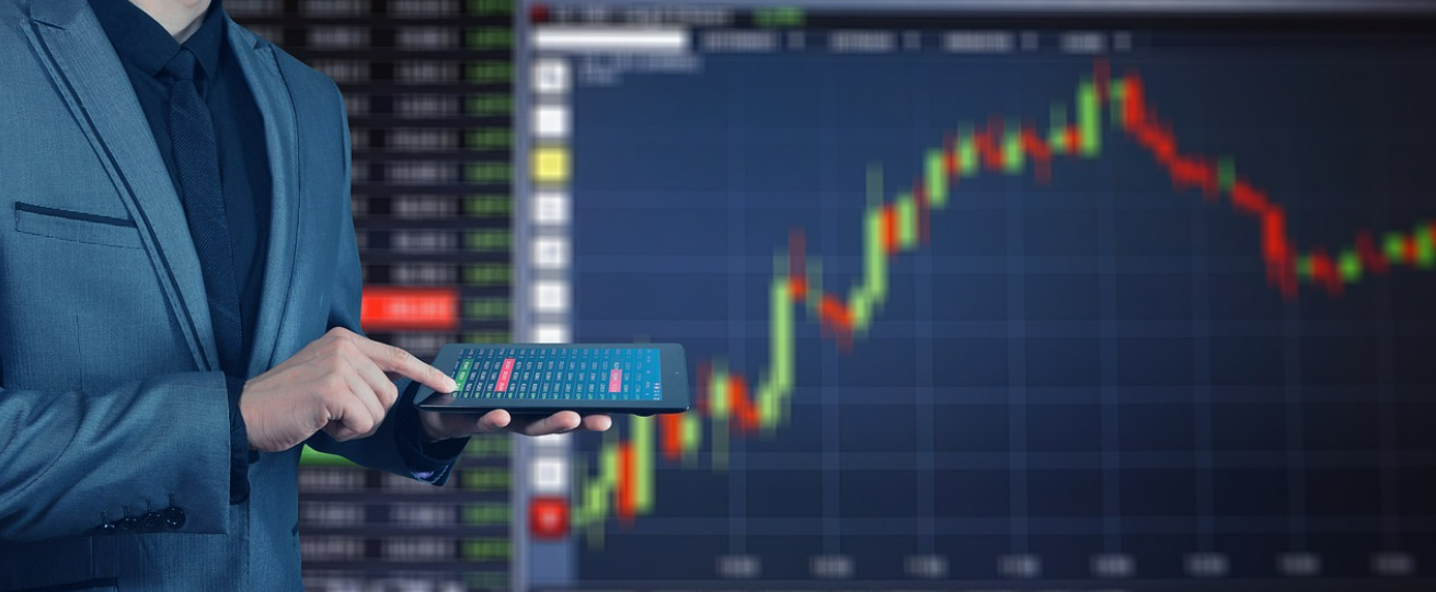 주식 차트 앞에 양복 입고 태블릿을 들고 서있는 남자