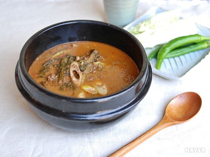 한로의 대표음식인 추어탕. 흰색 포가 깔린 상 위에 추어탕 한 뚝배기와 숟가락 하나, 정사각형의 접시 위에 배추 두장과 고추 3개가 있고 물 한잔이 있다.