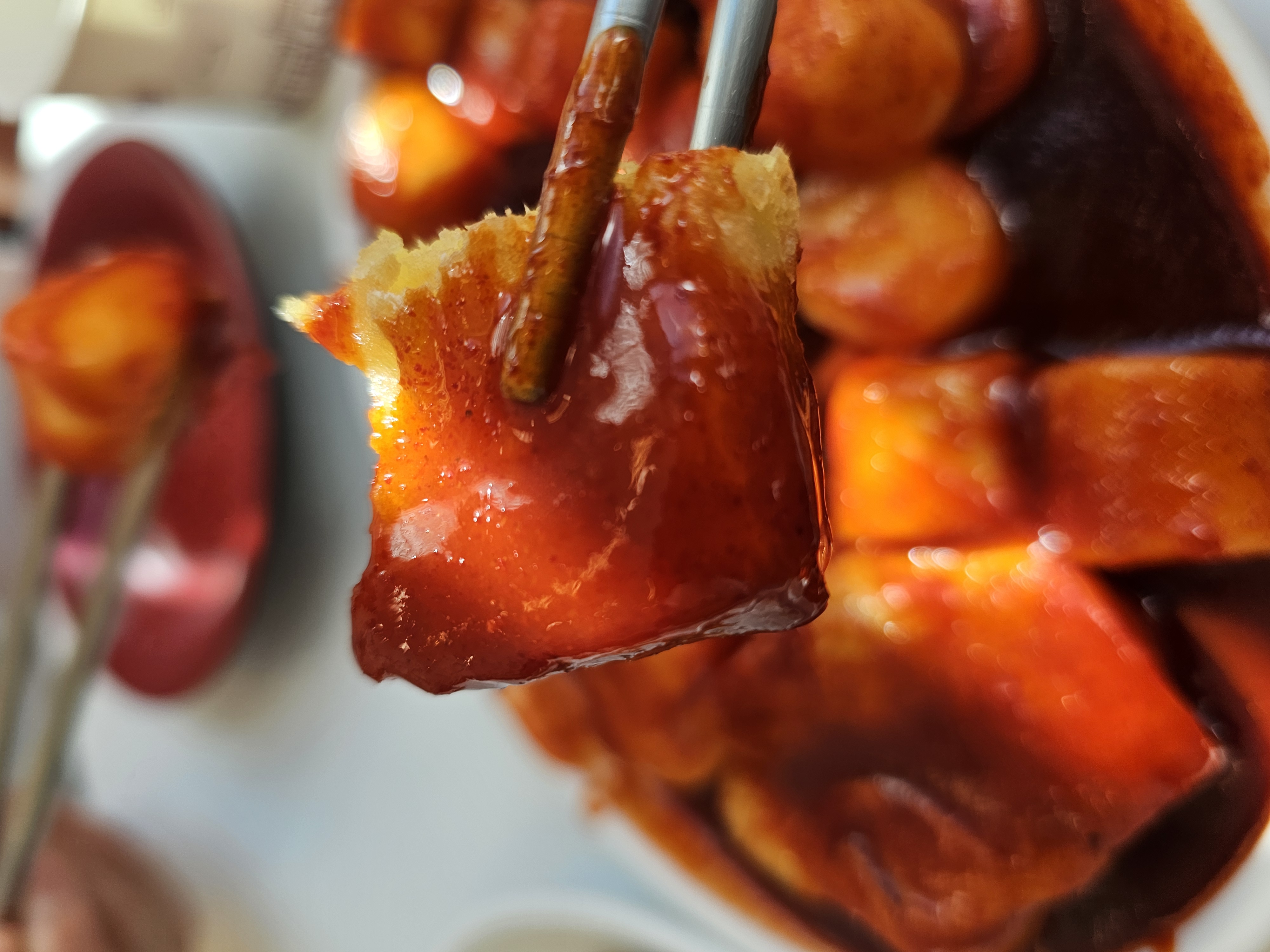 대왕 판 떡볶이 송도 본점 고구마튀김을 떡볶이 소스에 찍어 젓가락으로 들고 있는 모습