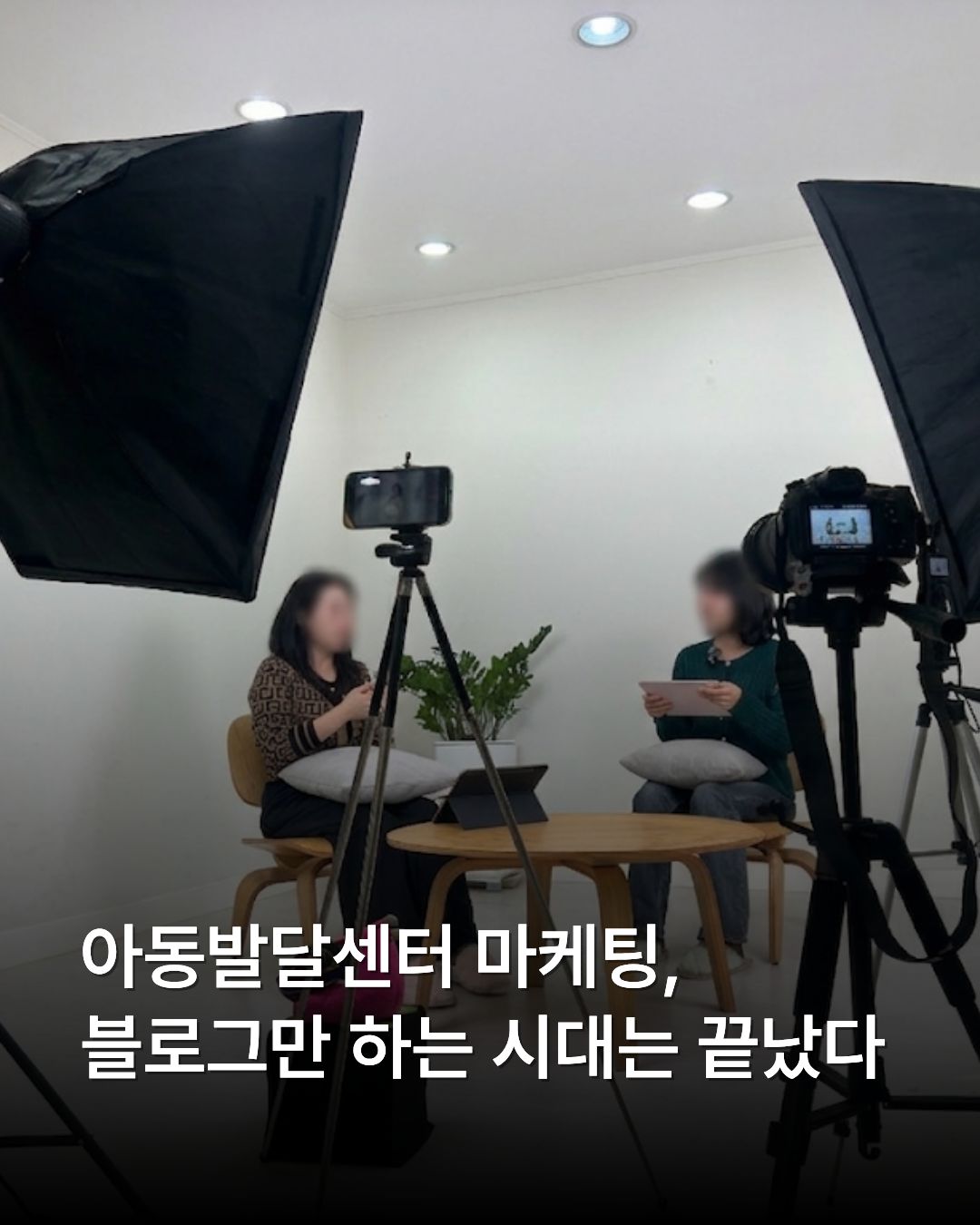전문 촬영 스튜디오에서 조명 장비와 삼각대에 거치된 카메라를 사이에 두고 두 여성이 앉아 인터뷰를 진행하고 있는 모습. 하단에는 '아동발달센터 마케팅, 블로그만 하는 시대는 끝났다'라는 흰색 문구가 적혀 있습니다.