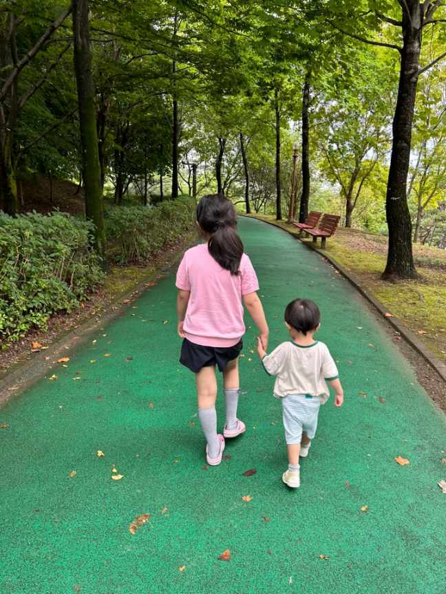 자녀 둘이 손잡고 숲속 공원길을 걷는 뒷모습