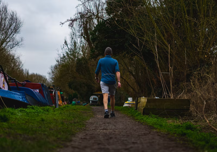 흙길 위를 걷는 남성의 뒷모습. 나무가 우거진 자연 속 산책로에서 걷기 운동을 실천하는 모습.