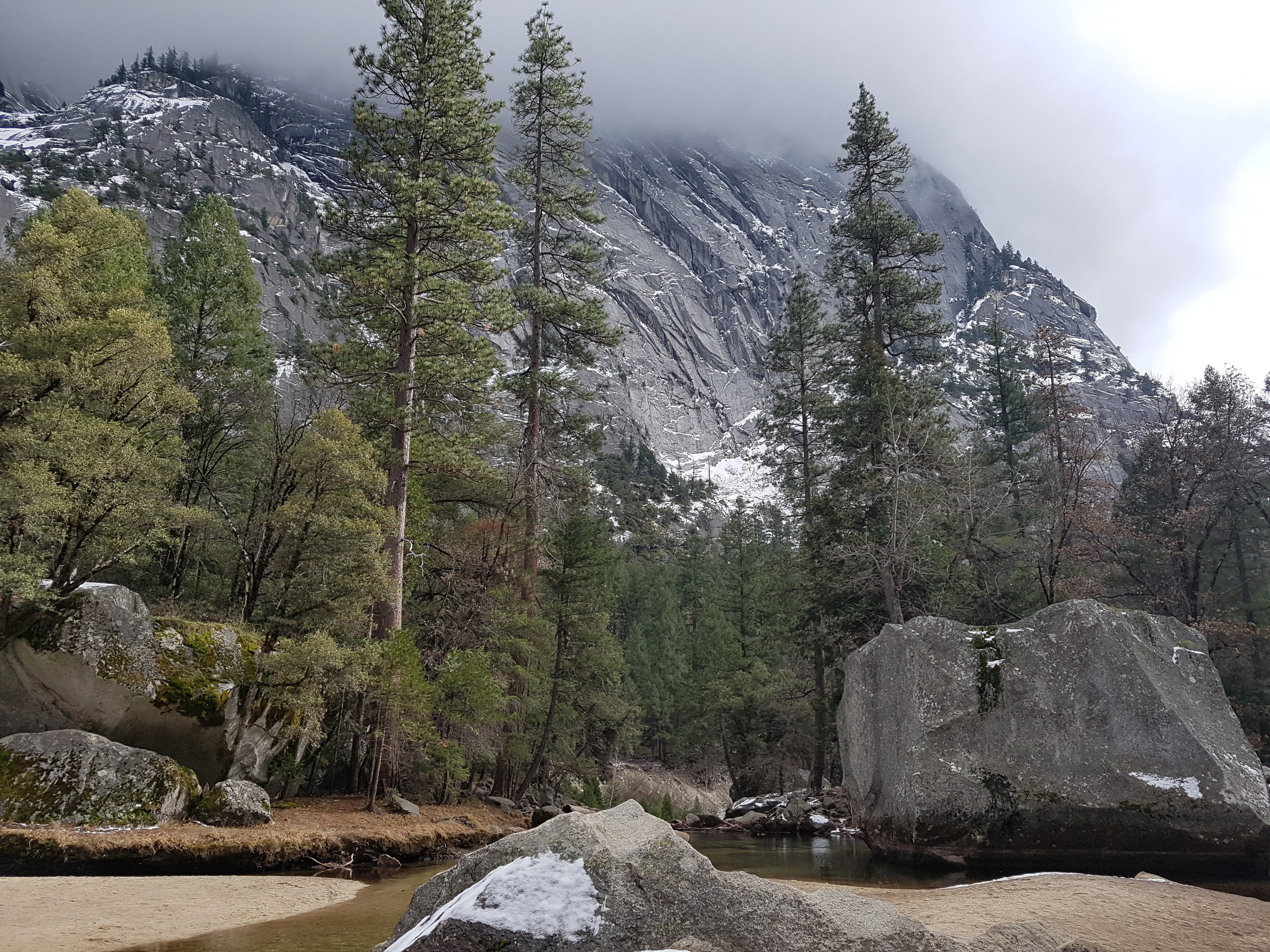 잔잔한 호숫가 바위와 눈 덮인 산비탈이 어우러진 요세미티의 겨울 풍경