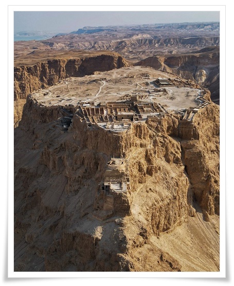 황량한 사막에 솟아오른 가파른 바위산 정상에 있는 요새의 전경. 웅장한 지질학적 풍경과 역사적 유적이 어우러진 인상적인 장면