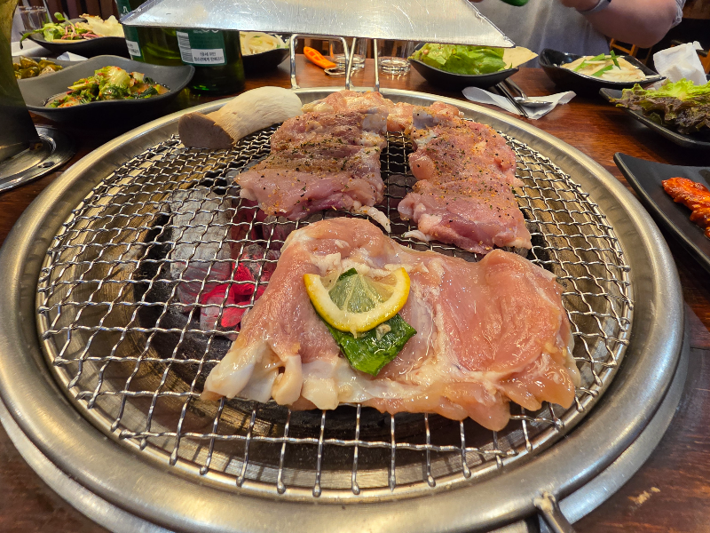 숯불 위에 닭갈비가 있다. 식탁위엔 반찬이 있다