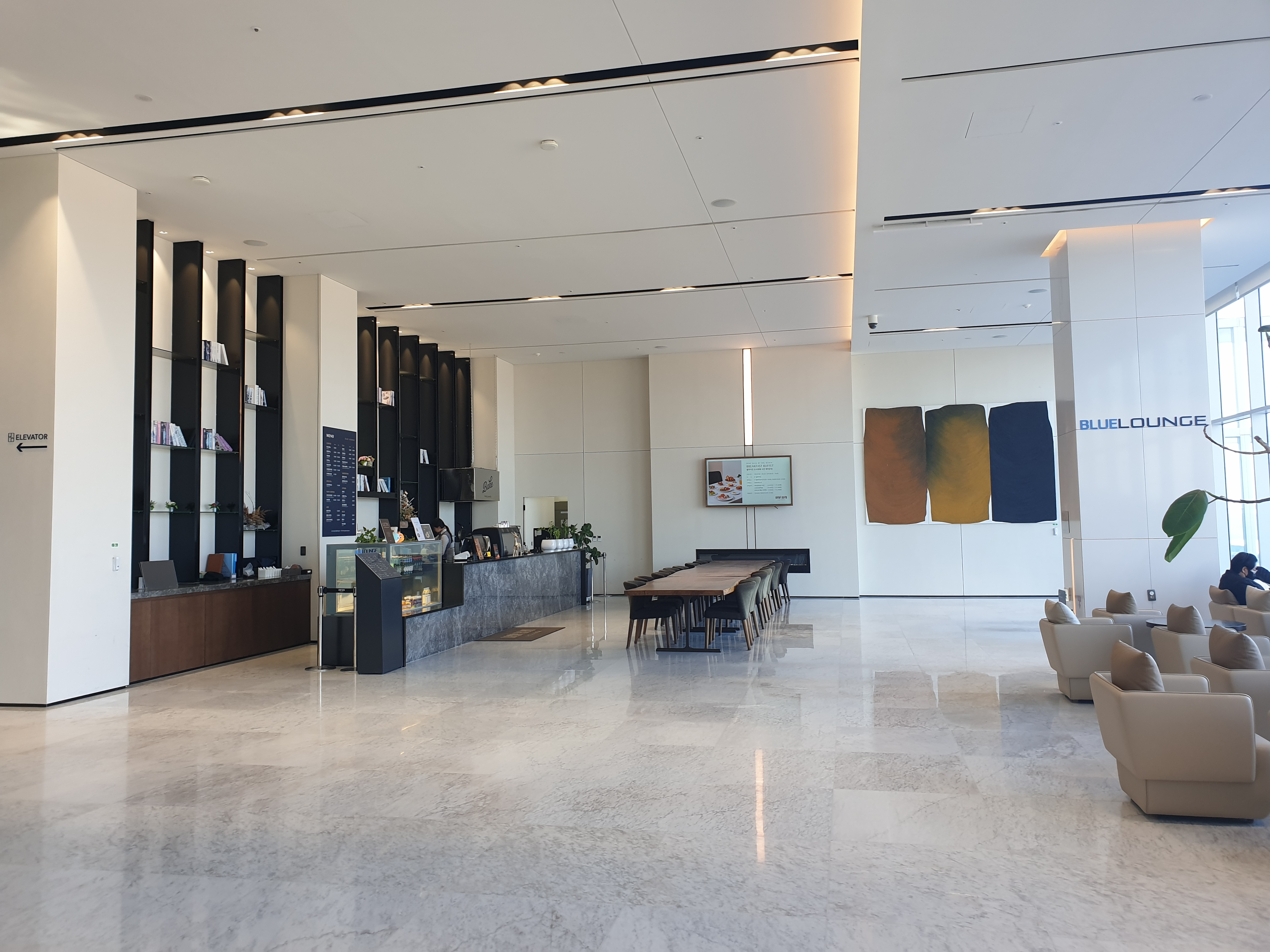 복도 왼쪽에는 카페(라운지)가 있고 오른쪽에는 회색 소파들이 있다.