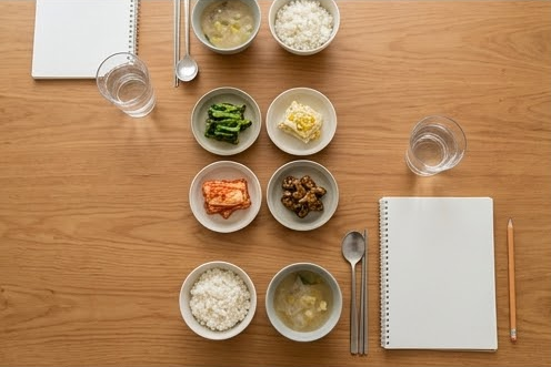 작은 반찬과 밥그릇, 빈 수첩이 놓인 식탁 위 모습