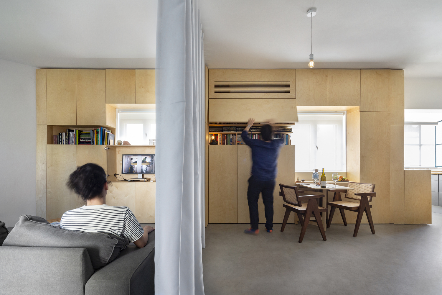 소파에-앉아있는-여성과-커튼이-쳐져있는-옆-공간에-남자가-물건을-꺼내고-있다