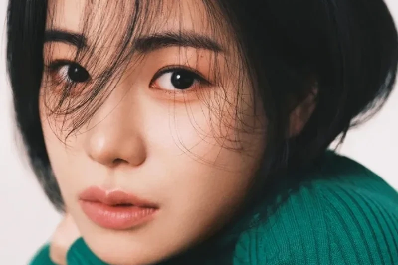 흰색을 배경으로 긴 검은 머리에 초록색 티를 입고 앉아 있는 배우 임지연