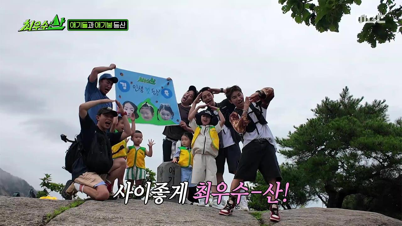 산 위 바위에서 최우수산 멤버들과 아이들이 현수막을 들고 기념사진을 찍는 방송 화면