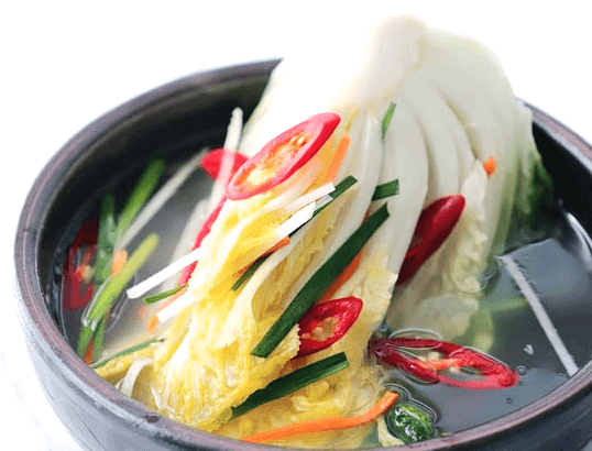 도자기 그릇에 담긴 하얀 백김치 반조각과 시원한 국물이 있고 빨간 고추 슬라이스들이 얹어있다.