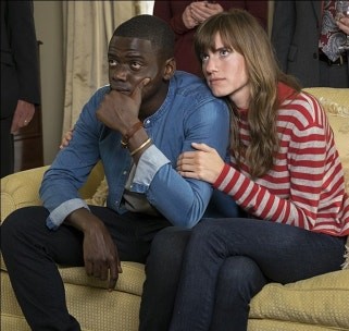 영화 '겟 아웃'의 한 장면에서 소파에 앉아 긴장한 표정으로 앞을 응시하는 흑인 남성과 그의 팔에 팔짱을 끼고 있는 백인 여성