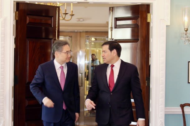 정장을 입은 두 남성이 열린 갈색 나무 문 사이로 대화하며 걸어나오고 있는 모습. 오른쪽 남성이 마코 루비오 국무장관으로 보인다.