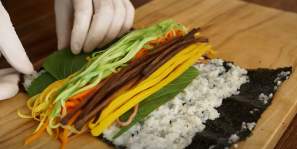 김에 밥을 올린 후 깻잎을 올린 뒤 그 후 나머지 재료들을 올리고 있습니다
