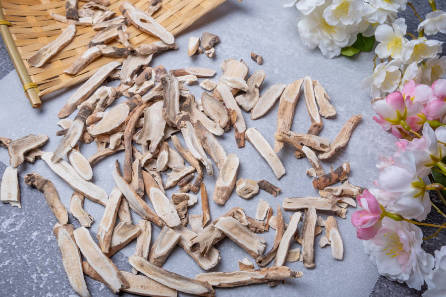 야생에서 채취를 한 백작약나무의 뿌리를 잘 세척한 후에 말린 것을 편으로 썰어 놓은 백작약을 회색바닥 위에 한지를 깔고 그 위에 대나무 키와 함께 놓아두고 옆에는 백작약 꽃을 두고 찍은 사진